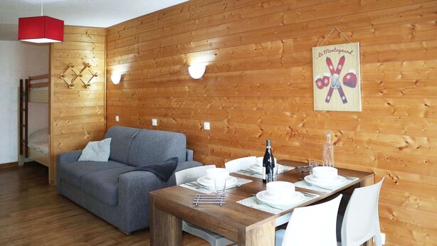 A cozy room with a wooden wall, a grey sofa, a wooden dining table set for four, and a red pendant light.