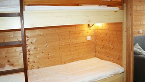 A wooden bunk bed with a mattress and a wall-mounted light.
