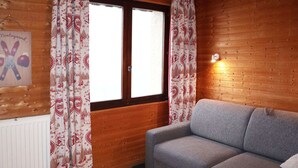 A cozy room with a grey sofa, wooden walls, and patterned curtains.
