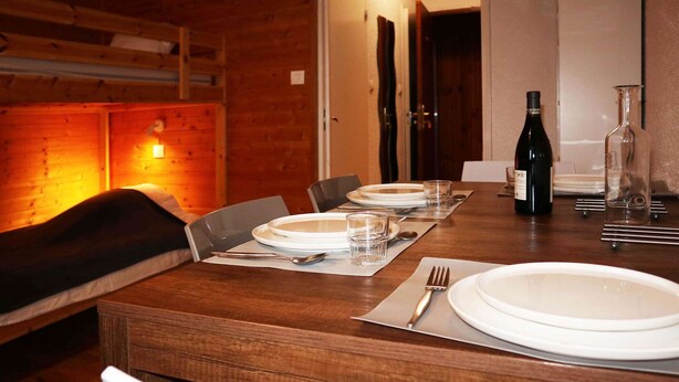 A wooden dining table set with white plates, glasses, and cutlery.