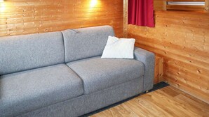 A grey sofa with a white pillow in a wooden cabin room with wooden walls and a red curtain.
