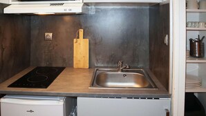 A compact kitchen with a microwave, an induction cooktop, a sink, and a small refrigerator.