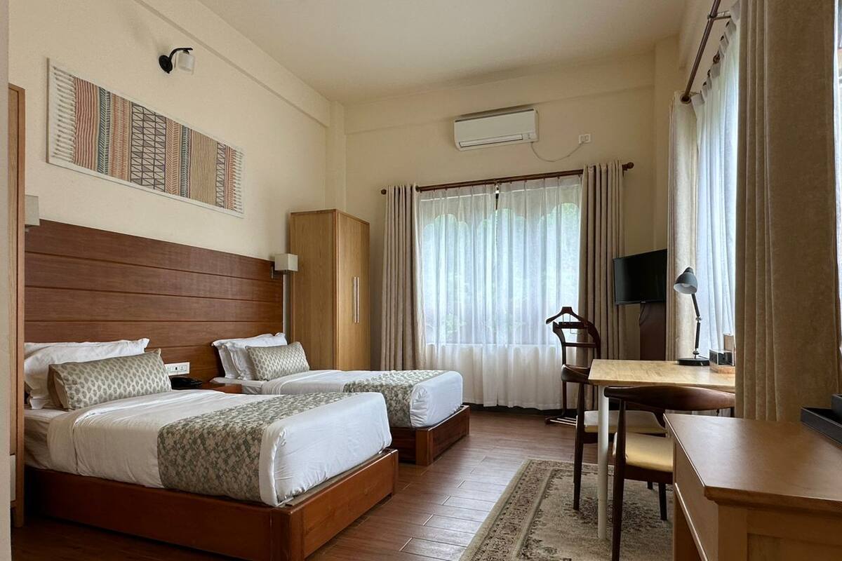 Une chambre d’hôtel avec deux lits, un bureau, une chaise, une télévision et une fenêtre avec des rideaux.