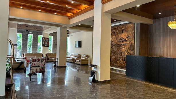 A spacious lobby with a polished marble floor, leather seating, a stone wall with artwork, and a wooden ceiling. - Legphel Hotel (Phuntsholing)