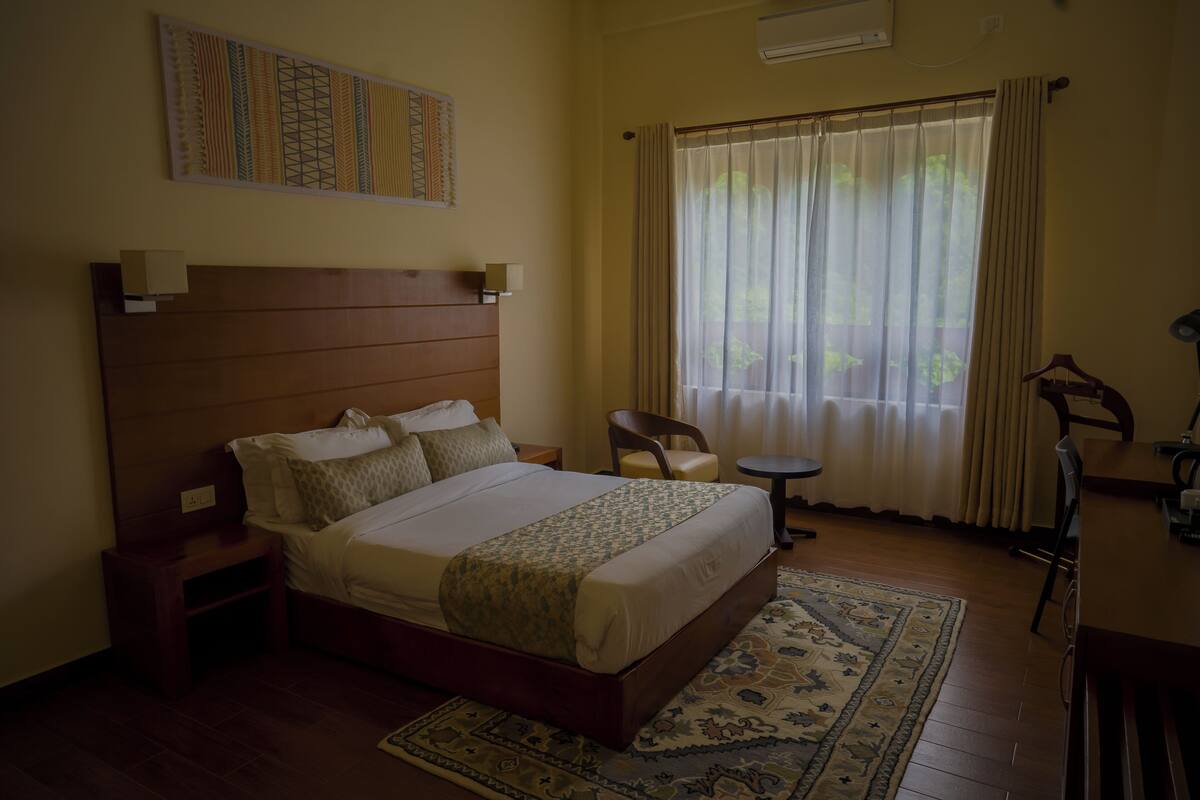 Une chambre d’hôtel avec un grand lit, une petite table, une chaise et une fenêtre avec des rideaux.