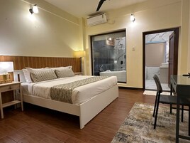 Un dormitorio con cama, mesita de noche, lámpara y vistas al baño y al pasillo.