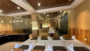 A dining area with a long table set for a meal, wooden paneling on the walls, and a stone accent wall. - Legphel Hotel (Phuntsholing)