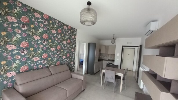 En stue med sofa, spisebord med stole, et køkken og en trappe.