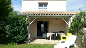 Een huis met een overdekte patio, een kleine tafel met stoelen, en een gele stoel.