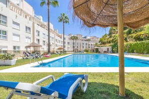 Une piscine entourée de chaises longues, de palmiers et d’un bâtiment doté de balcons.