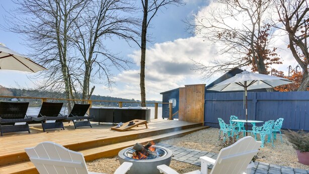 An outdoor patio with Adirondack chairs, a fire pit, and a deck overlooking a body of water. - Victorian Lake Oasis (Lake Huntington)