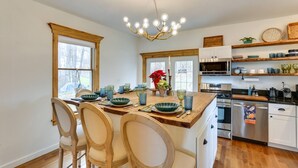 A kitchen with wooden cabinetry, a central island with chairs, a chandelier, and a view through large windows. - Victorian Lake Oasis (Lake Huntington)