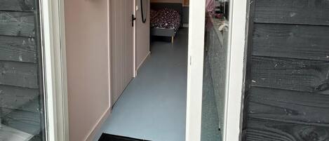 A narrow hallway leading to a bedroom with a bed and a window.