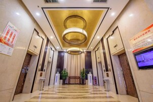 A hotel lobby with a check-in counter, a reception desk, and a large digital screen on the wall.