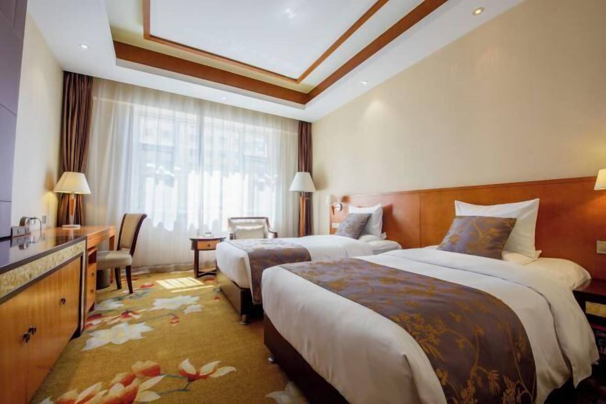 A hotel room with two beds, a desk, a chair, and a window with curtains.