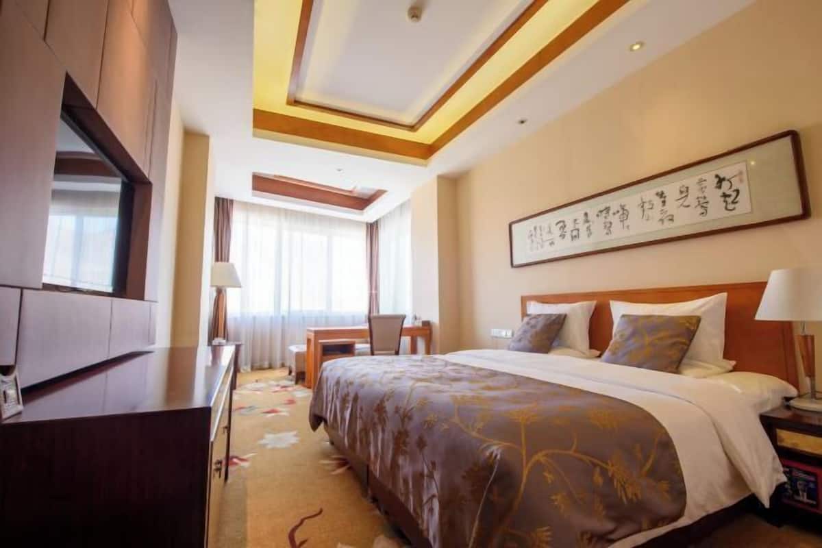 A hotel room with a large bed, a desk, a TV, and a wall with calligraphy.
