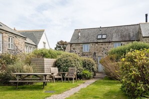 A stone building with a sloped roof, a wooden bench, and chairs in a garden area.