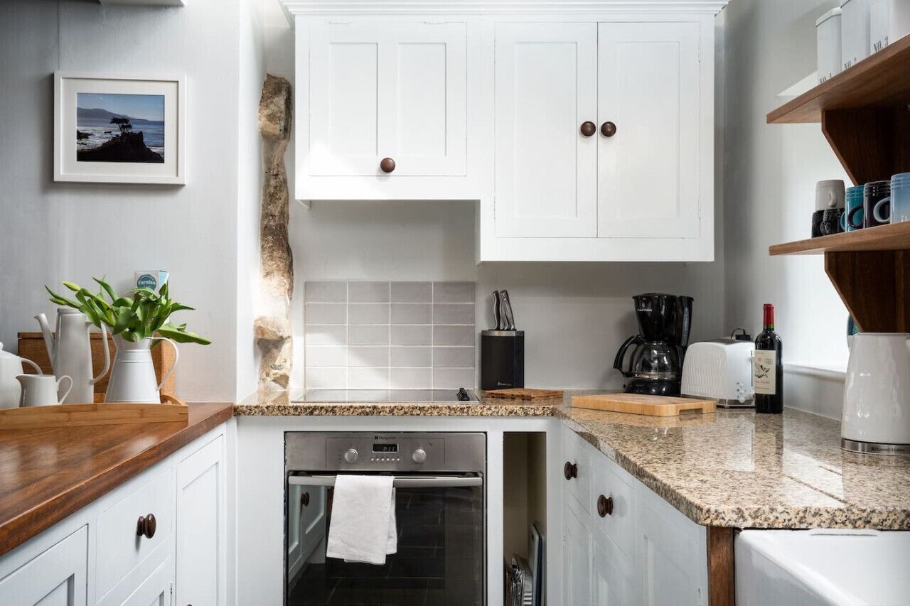 Una cocina con armarios blancos, encimera de granito, cafetera, tostadora y una botella de vino.