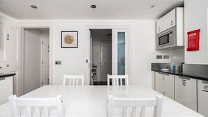 A modern kitchen with white cabinetry, a black countertop, and a microwave. There is a fire blanket on the wall and a framed picture above the sink. - The Tachbrook at No. 195: 6-Bed Historic Townhouse | Victoria (London)