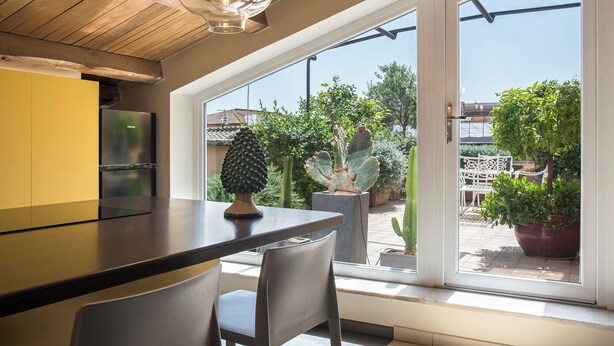 A modern kitchen with a large window, a dining area with chairs, and a cactus sculpture. - Exclusive Roman Attic: Between Vatican, Trastevere & Piazza Navona (Roma)