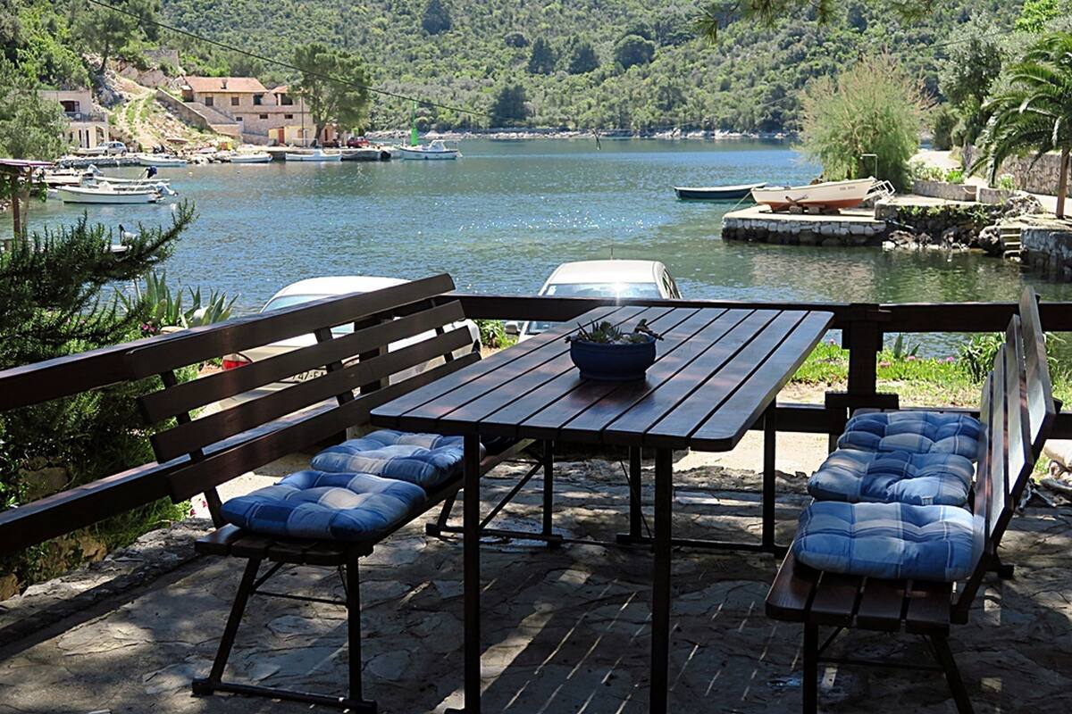 A wooden deck with a table and benches overlooking a lake with boats and houses in the background.