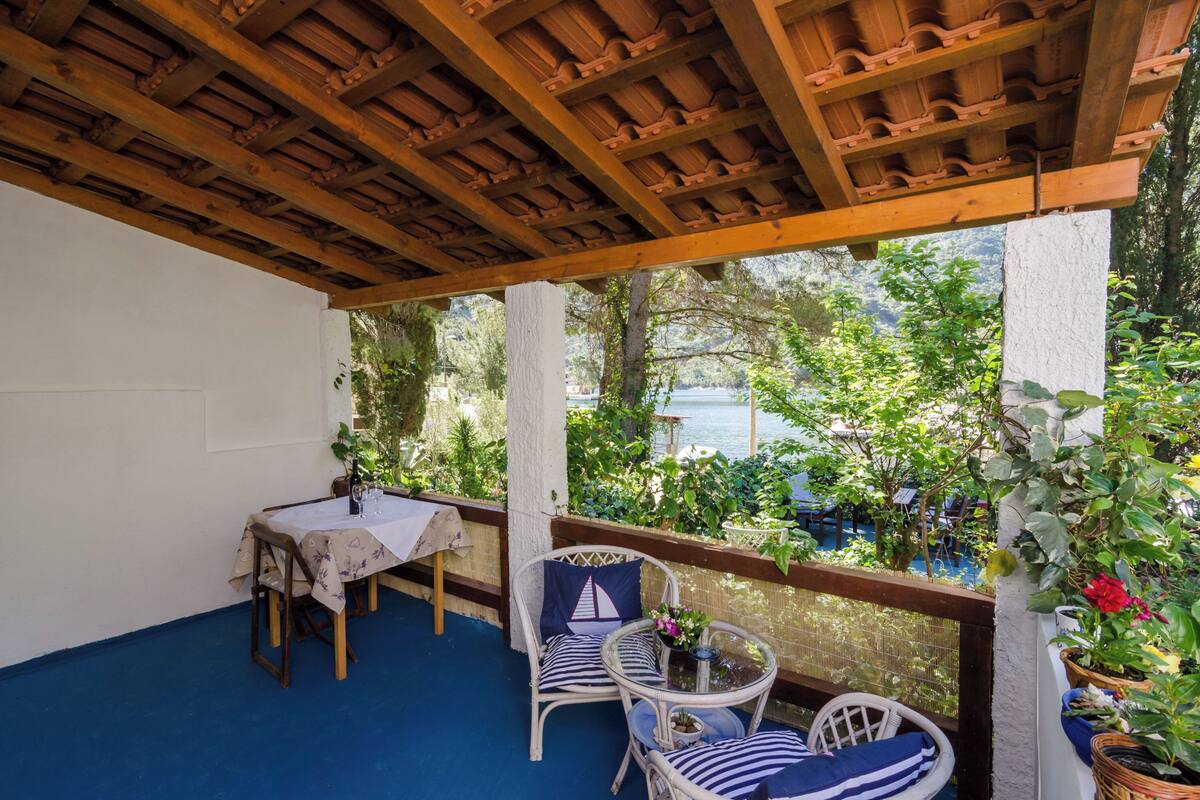 A covered patio with a table and chairs, a view of greenery and a body of water.