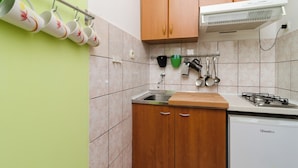 A kitchen with wooden cabinets, a gas stove, a dishwasher, and a hanging rack with cups. - Apartments Vera (Mljet)