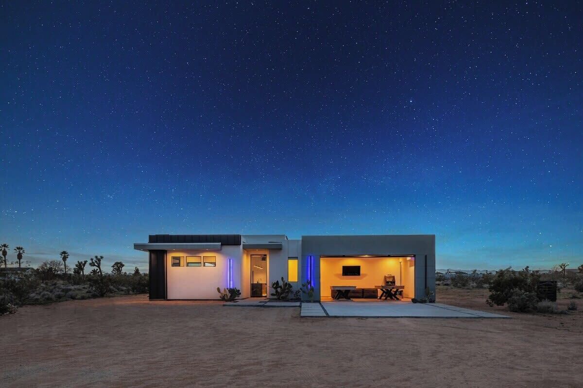Une maison moderne à deux étages, dotée d’un toit plat, d’un patio et offrant, en arrière-plan, un paysage désertique.