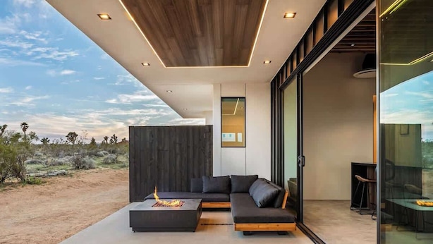 Una sala de estar moderna con un sofá modular grande, una mesa de centro con chimenea y un ventanal de vidrio que da a un espacio exterior.