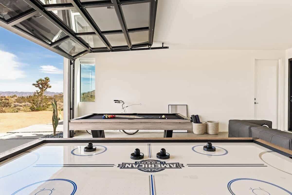 A pool table with a clear view of the surrounding area, including a sofa and a window with a view of the desert landscape.