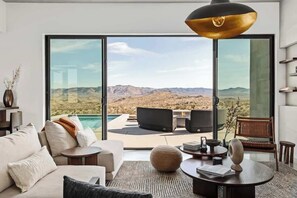 A modern living room with a large window offering a view of a desert landscape. - Revolve • Luxury Oasis with View, Pool, Spa, Sauna (Yucca Valley)