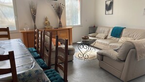 A living room with a sofa, a dining table with chairs, a TV mounted on the wall, and a window. - 4 Bedroom Apartment in Camblain-ChÃ¢telain (Camblain-Châtelain)