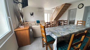 A compact living space with a dining area, sofa, staircase, and a flat-screen TV mounted on the wall. - 4 Bedroom Apartment in Camblain-ChÃ¢telain (Camblain-Châtelain)
