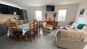 A modern living room with a dining area, a sofa, a TV mounted on the wall, and a kitchen area with cabinets and a countertop. - 4 Bedroom Apartment in Camblain-ChÃ¢telain (Camblain-Châtelain)