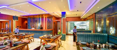 Un restaurant doté de nombreuses tables et de plusieurs coins repas, d’un espace d’accueil et offrant une vue par la fenêtre.