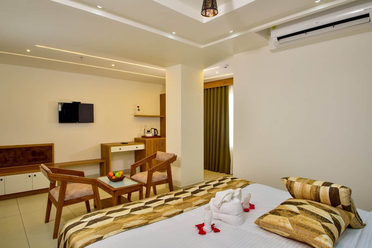 A hotel room with a bed, a desk, a chair, a TV, and an air conditioning unit.