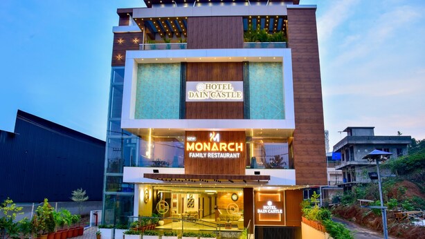 Et moderne hotel med et tydeligt skilt, der viser 'Hotel Dain Castle', og en 'Monarch Family Restaurant' nedenfor.