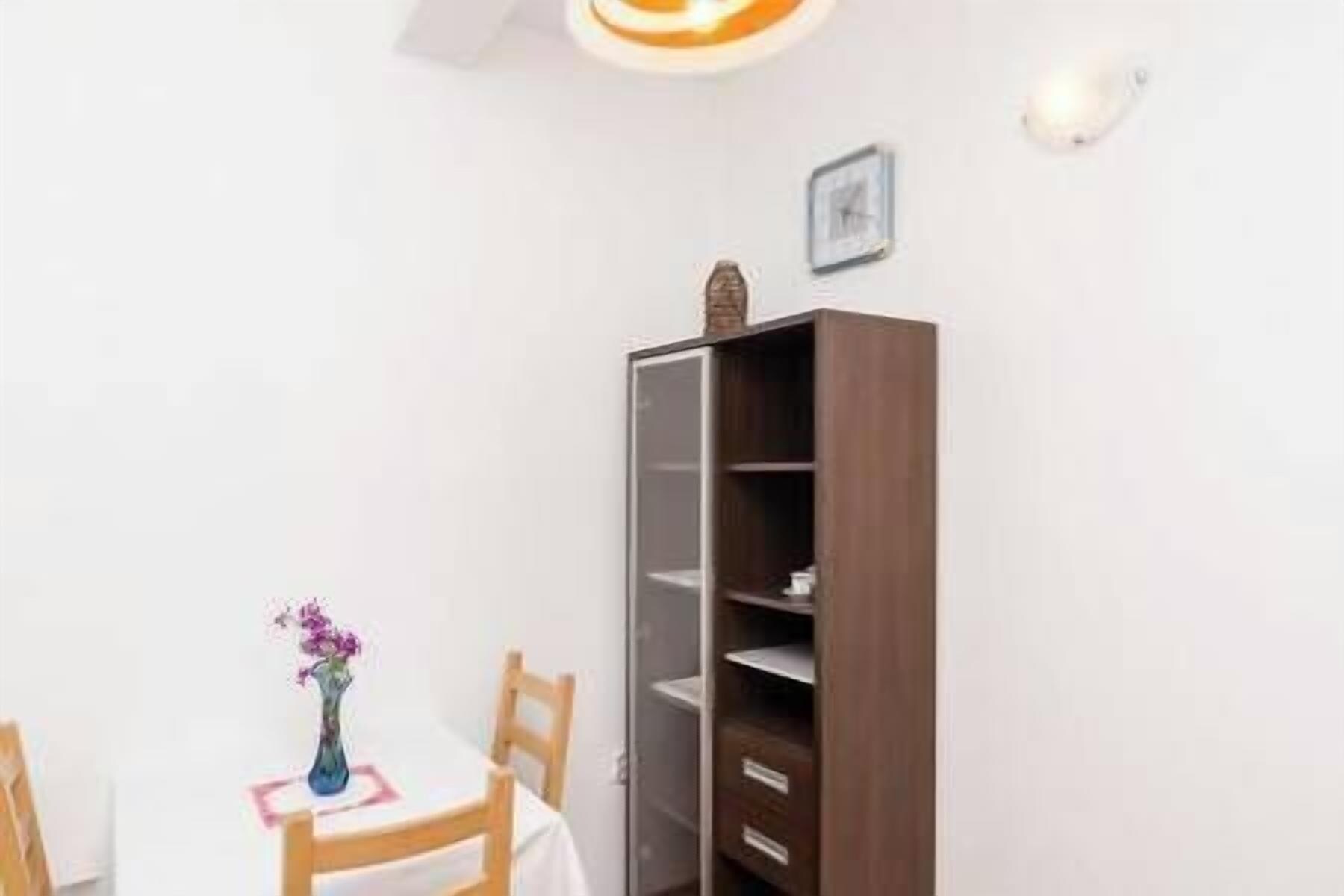 Una habitación con una mesa de comedor, sillas, un florero con flores y un aparador de madera alto con estantes abiertos.