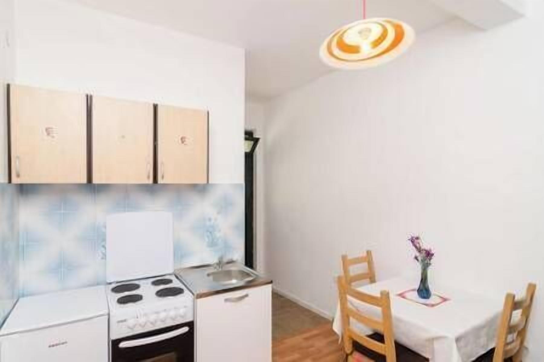 A compact kitchen with a stove, sink, and wooden cabinets. There is a dining area with a table and chairs, and a pendant light above the table.