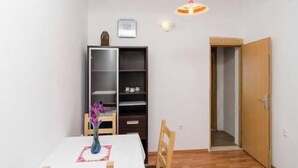 A small, sparsely furnished room with a wooden floor, a white table, a chair, a bookshelf, and a door leading to another room. - Apartments Felix Mljet (Mljet)