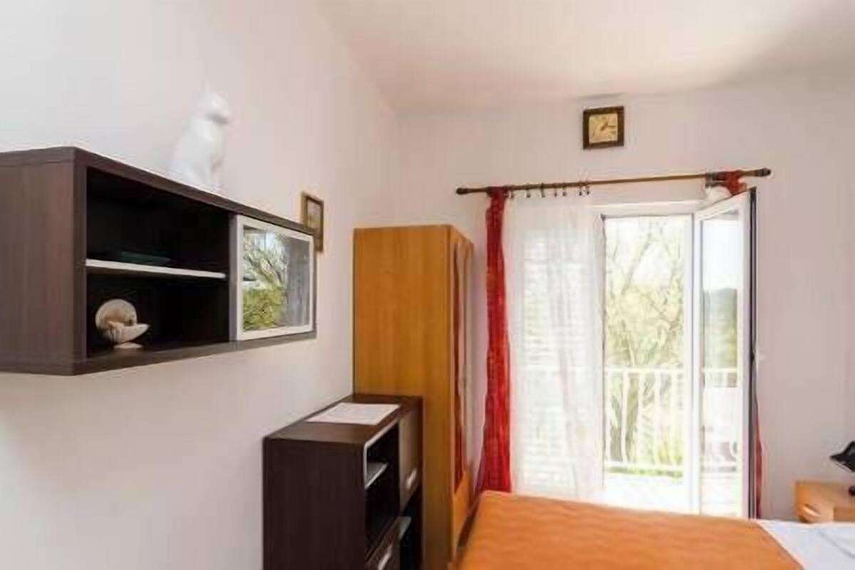Ein Schlafzimmer mit einem Bett, einem Holzschrank, einem Regal mit einem Bild und einem Fenster mit Vorhängen.