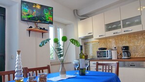 Un coin repas avec une nappe bleue, un téléviseur fixé au mur et des appareils de cuisine.