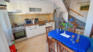 Une cuisine moderne avec des meubles blancs, une table à manger recouverte d’une nappe bleue et un escalier menant à une mezzanine.