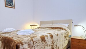 Un lit bien fait, recouvert d’une couverture marron et blanche, une lampe de chevet et une petite table de nuit en bois sur laquelle repose un livre.