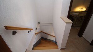 Un escalier en bois, avec des marches et des rampes, menant à une chambre à coucher équipée d’un lit et d’une lampe.