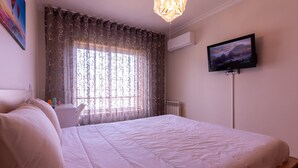 Un dormitorio con cama, escritorio, silla, televisor y ventana con cortinas.
