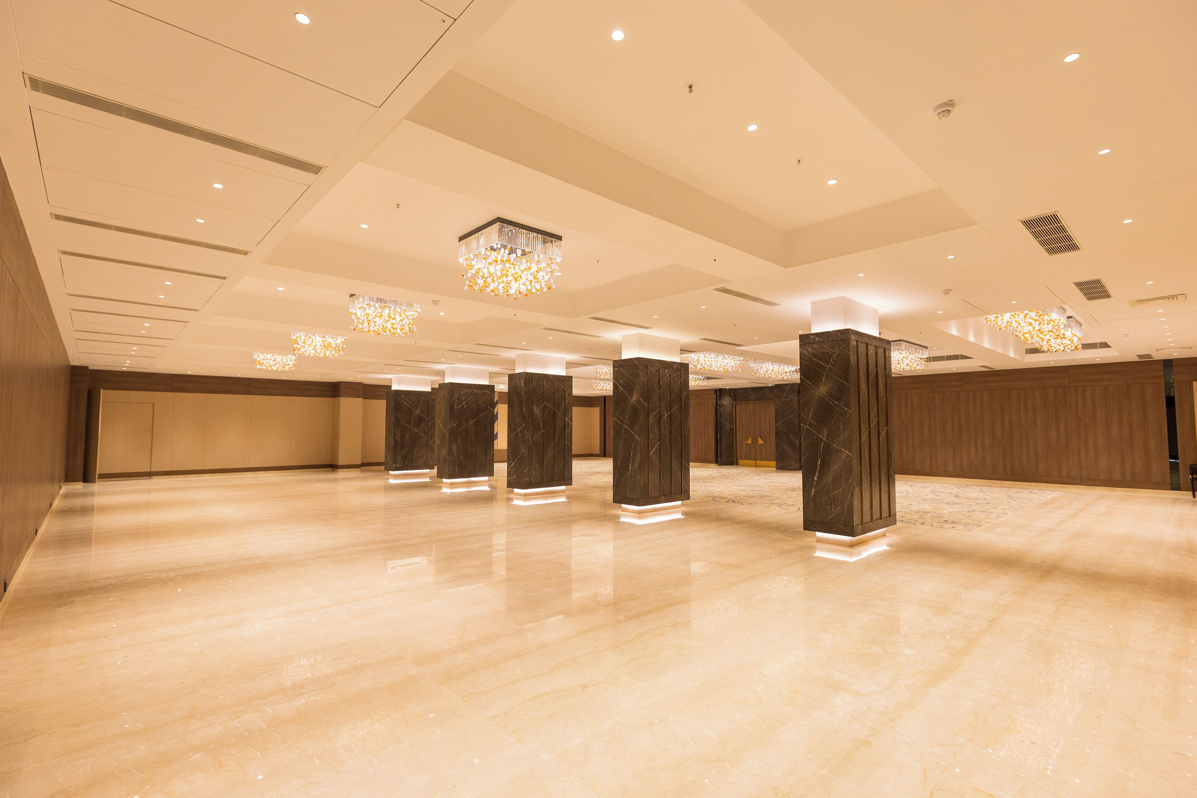A spacious, well-lit hotel lobby with marble flooring, tall columns, and decorative chandeliers.