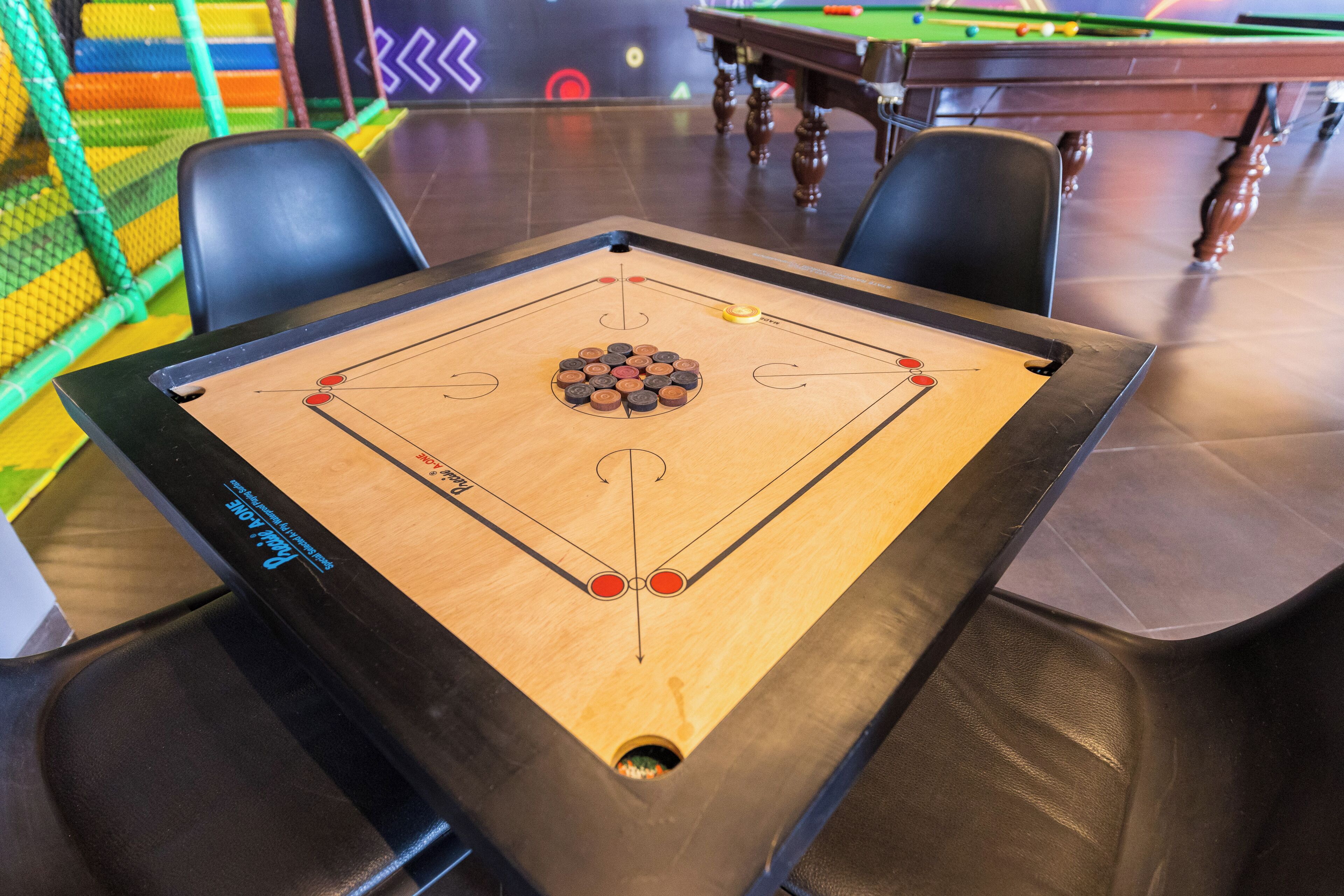A shuffleboard table with a wooden surface and a central scoring area, surrounded by chairs.