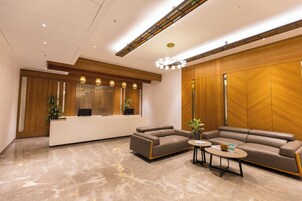 A modern reception area with a reception desk, two sofas, a coffee table, and a decorative chandelier.