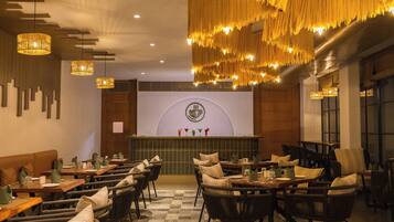 A restaurant with a modern interior, featuring wooden tables and chairs, hanging lights, and a projection screen on the wall.